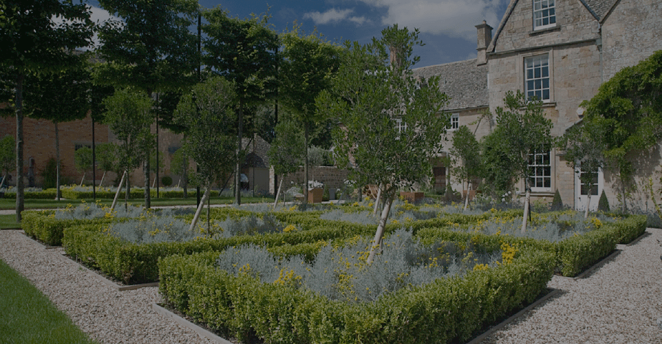 Estate gardens featuring rectangular hedges with flowers and a tree in each rectangle, designed by Cotswold Estates and Gardens.