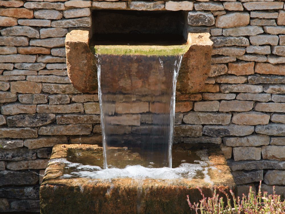 shipton Oliffe Water pouring out of a stone fountain in the redesigned Shipton Oliffe garden by Cotswold Estates and Gardens.