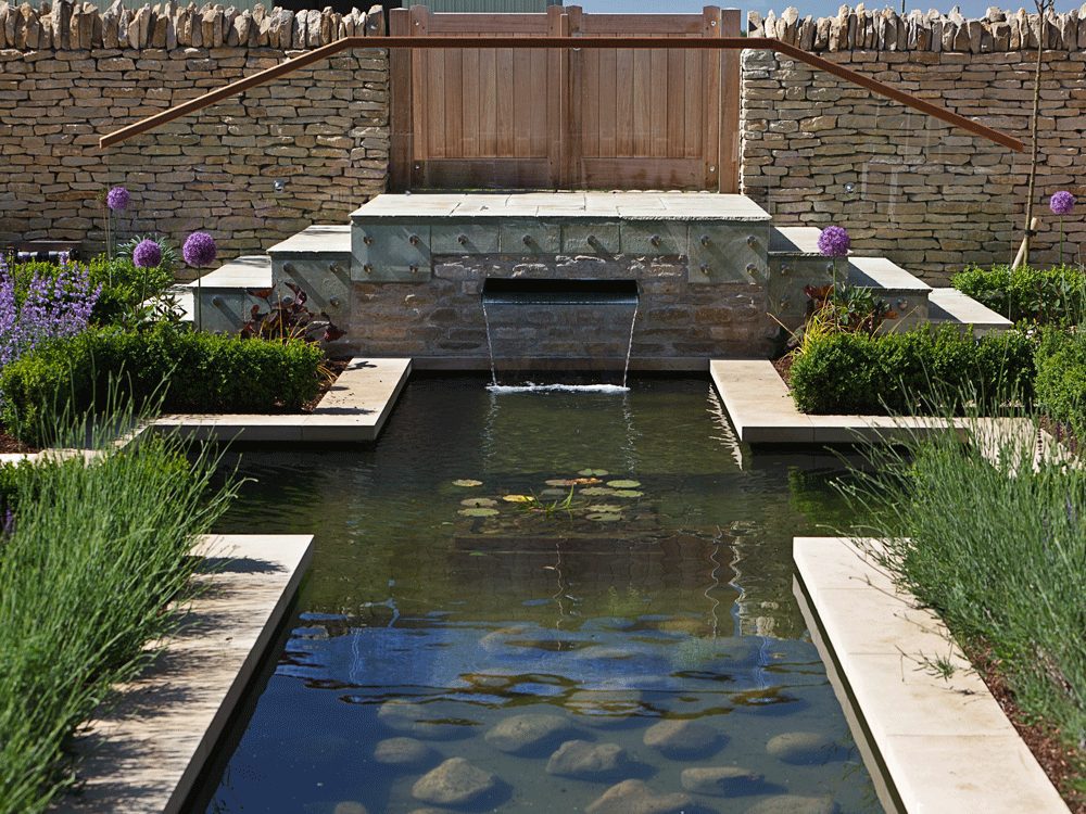 A wide-angle shot of a waterfall flowing into a pond, surrounded by lush plants, created by Cotswold Estates and Gardens.